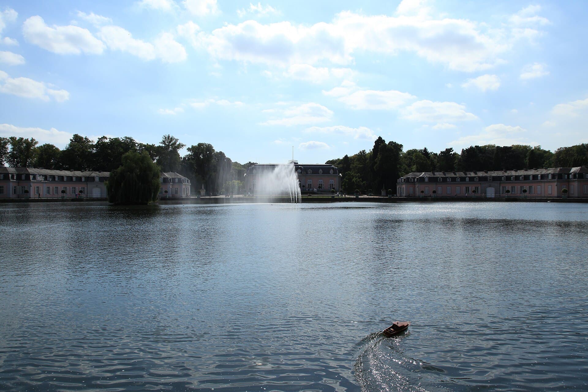 Schloss Benrath hinter dem Schlossweiher mit Fontäne, von der Benrather Schloßallee aus gesehen