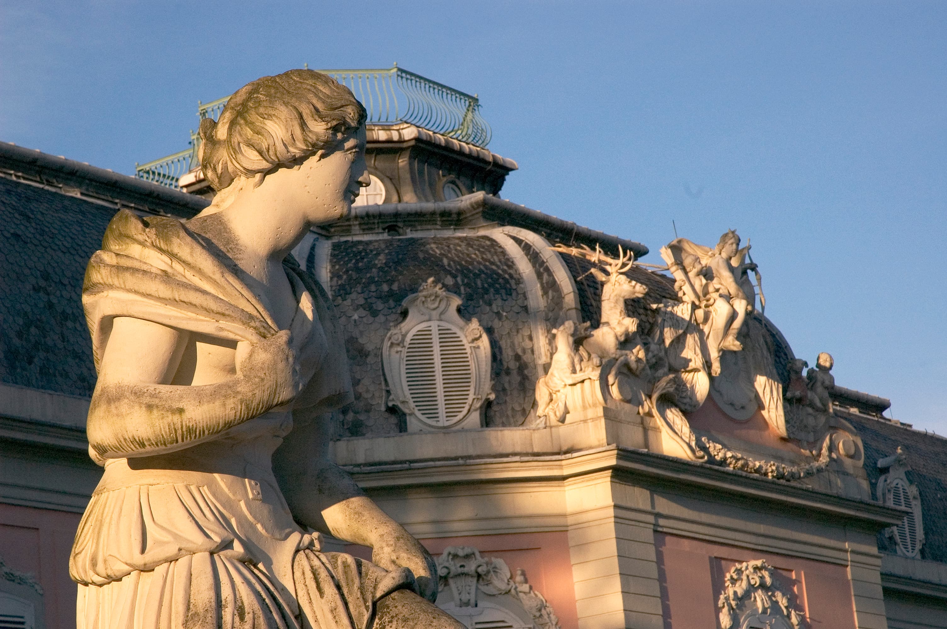 Statue vor dem Mansarddach des Corps de Logis von Schloss Benrath im warmen Abendlicht
